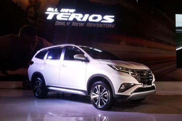 Sebuah SUV Daihatsu Terios berwarna putih dipajang di atas panggung mengilap di sebuah pameran otomotif dalam ruangan, dengan tulisan "All New Terios Daily New Adventure" menyala pada latar belakang gelap di belakang kendaraan.