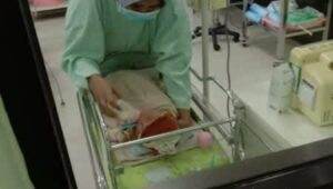Seorang petugas kesehatan berhijab dan masker merawat bayi yang baru lahir di dalam inkubator di kamar rumah sakit yang penuh dengan peralatan medis.