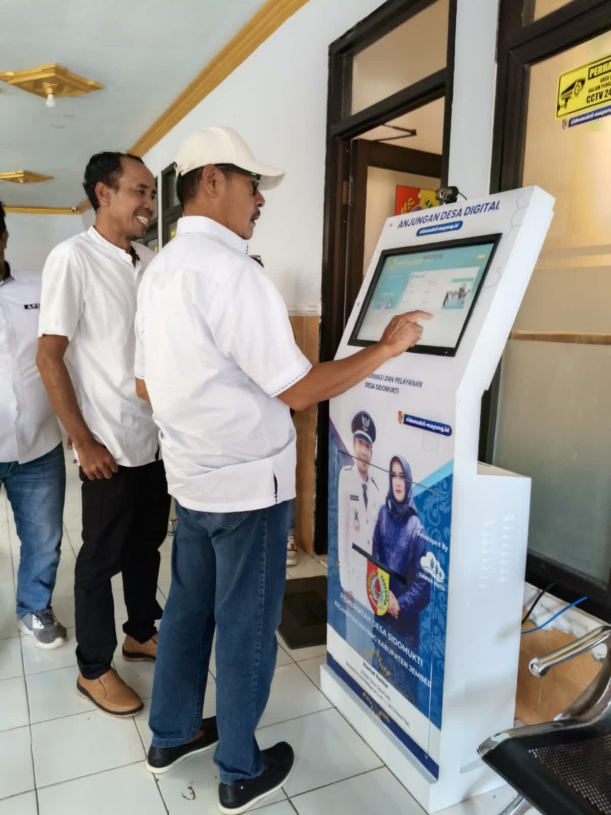 Djoko Susanto Wabup Jember mencoba mesin anjungan pelayanan mandiri semabari mengisi Buku Tamu di Dampingi Kades Sidomukti Sunardi Hadi (Foto Istimewah : Surya )