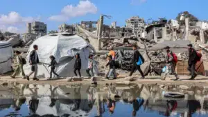 Orang-orang berjalan melewati tenda perlindungan di dekat reruntuhan bangunan yang runtuh di bagian barat Kota Gaza pada tanggal 15 April. Omar Al-Qattaa/AFP via Getty Images