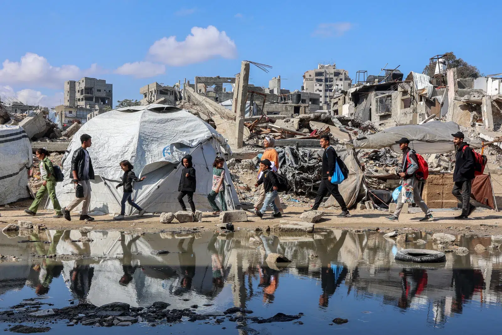 Orang-orang berjalan melewati tenda perlindungan di dekat reruntuhan bangunan yang runtuh di bagian barat Kota Gaza pada tanggal 15 April. Omar Al-Qattaa/AFP via Getty Images